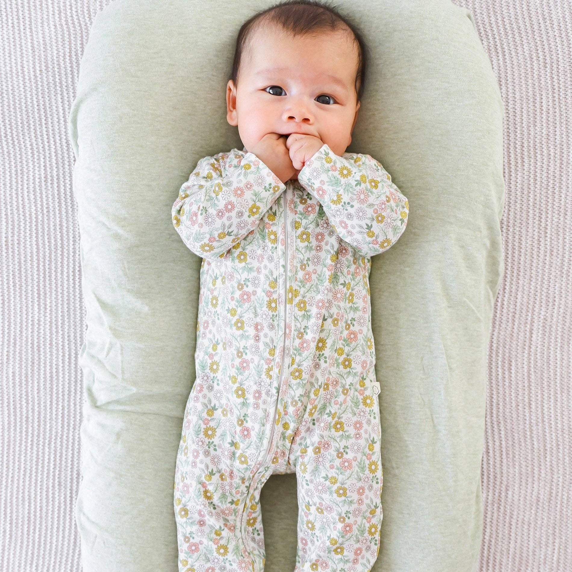 Baby in a floral onesie lying on a soft pillow