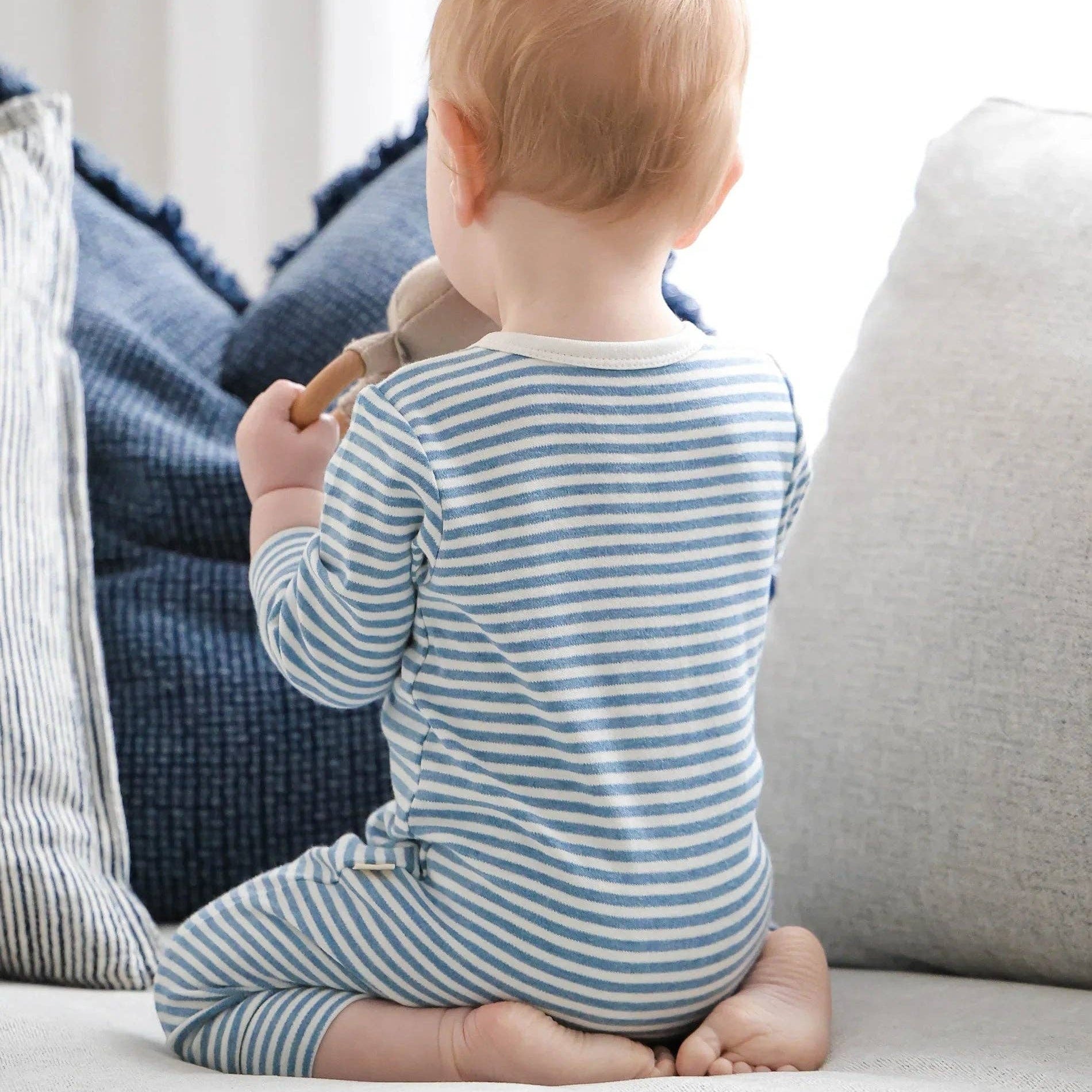 Baby in a striped onesie sitting on a couch