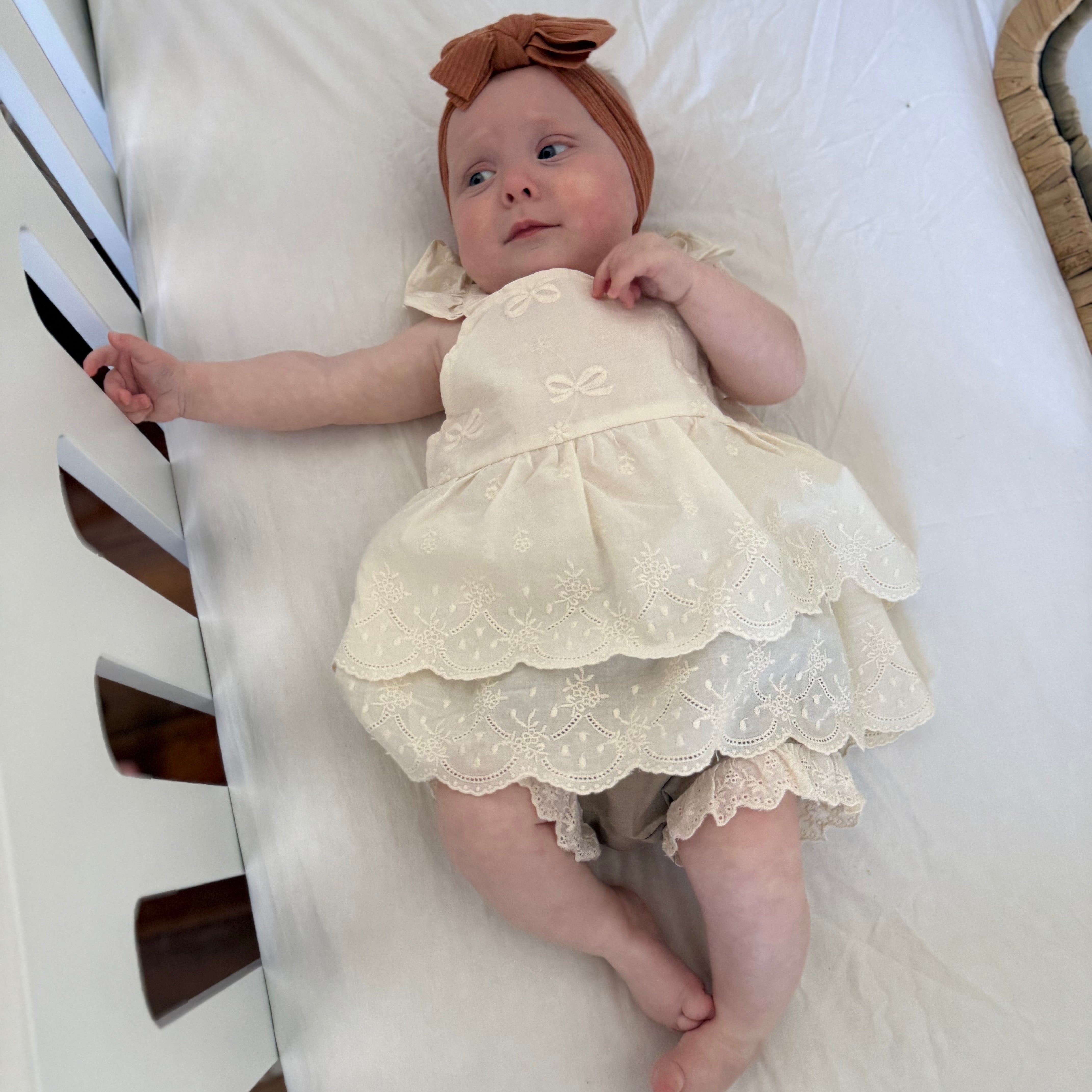 Baby in a white lace dress lying on a white blanket