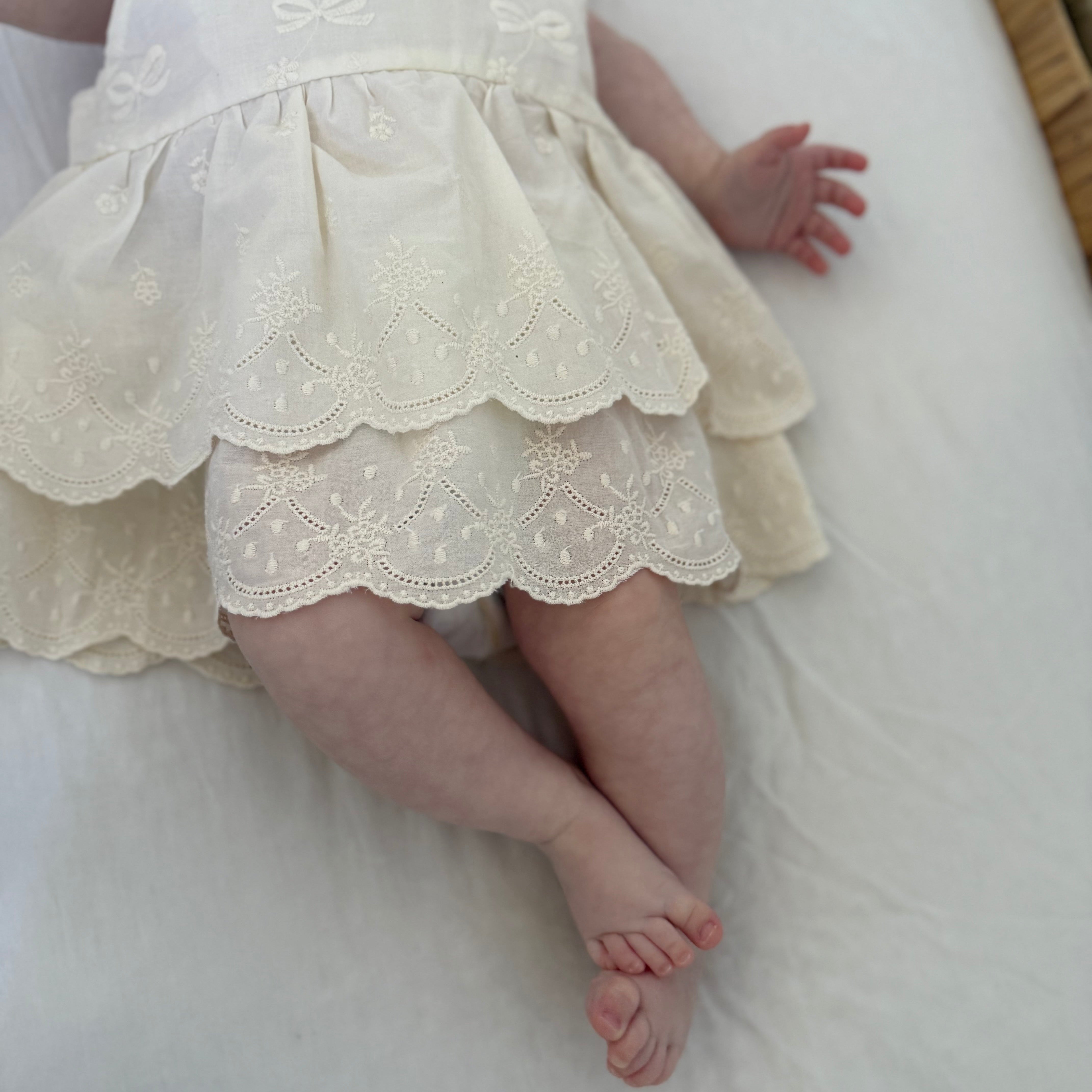 Baby in a white lace dress lying on a white surface