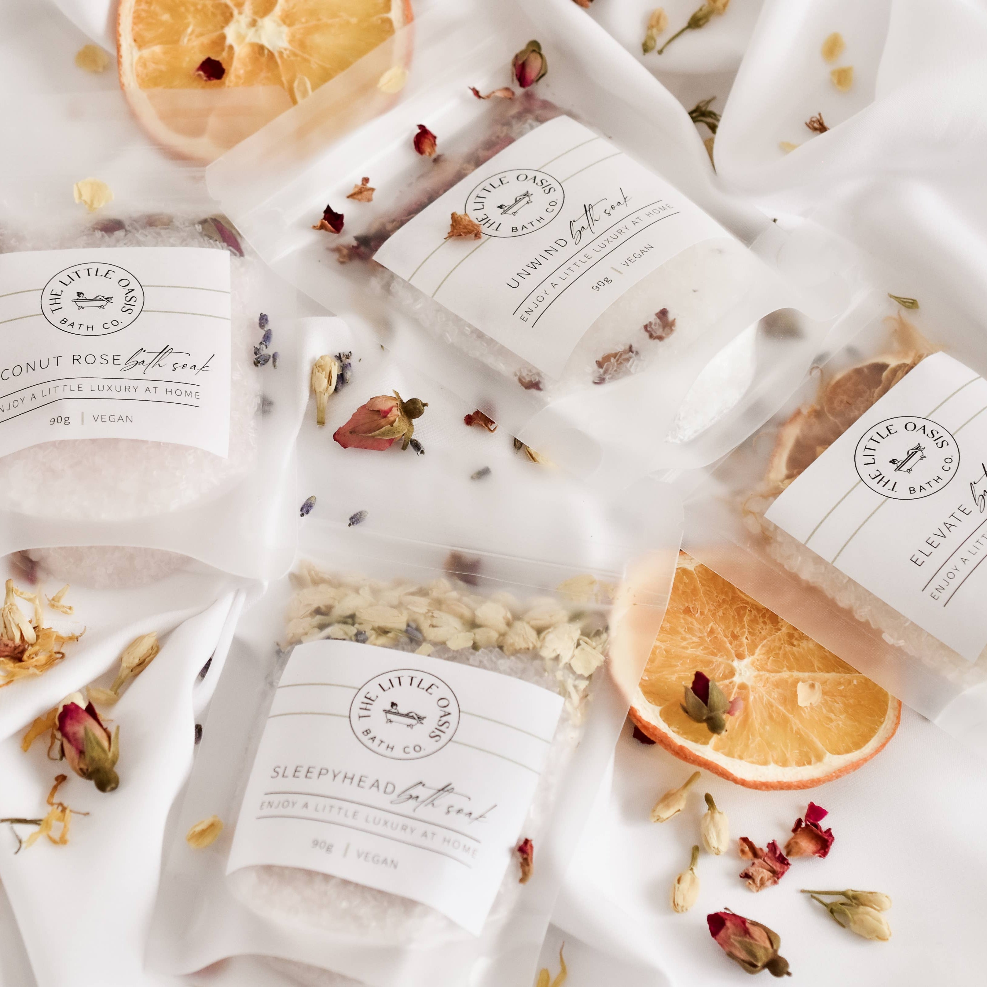 Various bath salts with labels and orange slices on a white background