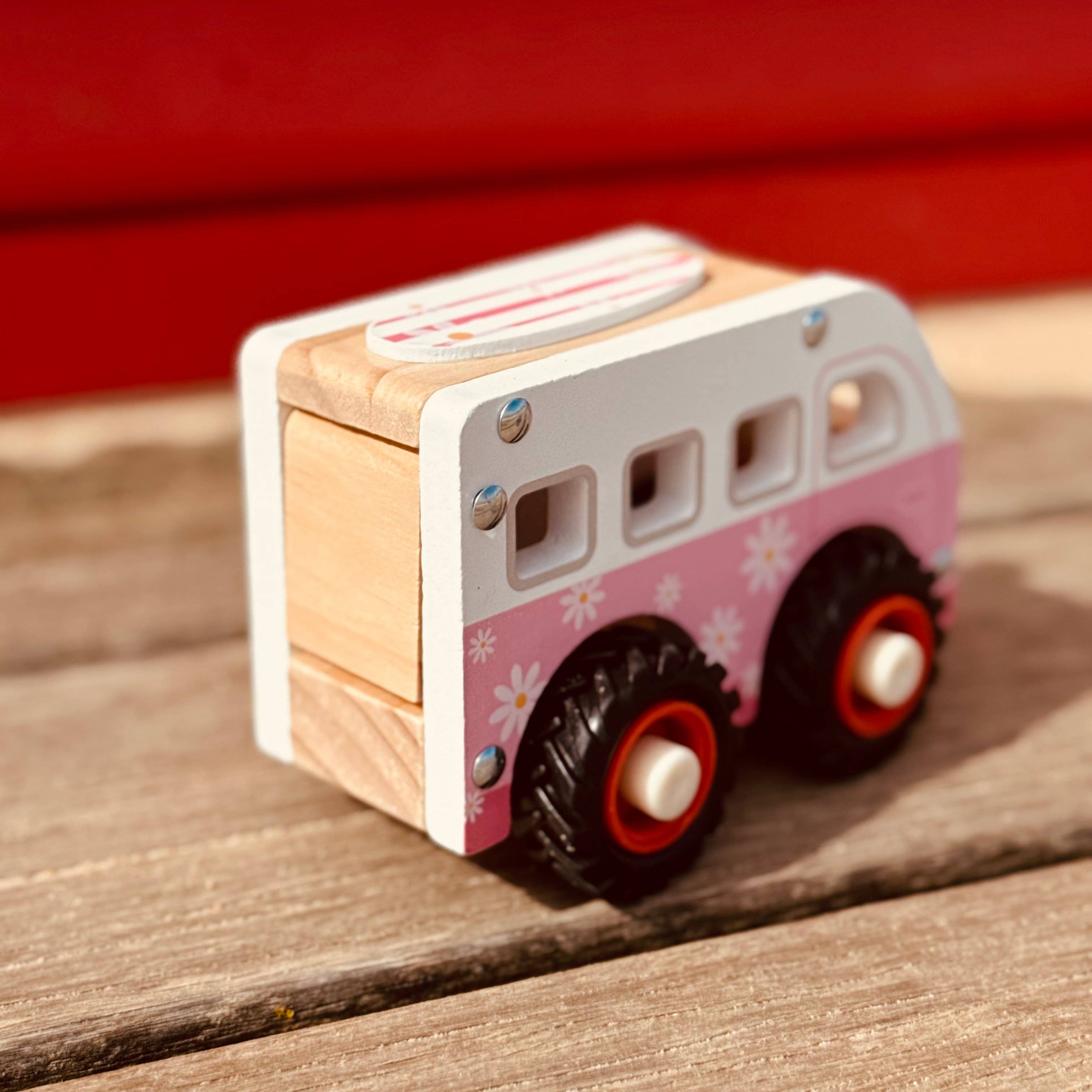 Wooden toy bus with pink floral design on a wooden surface