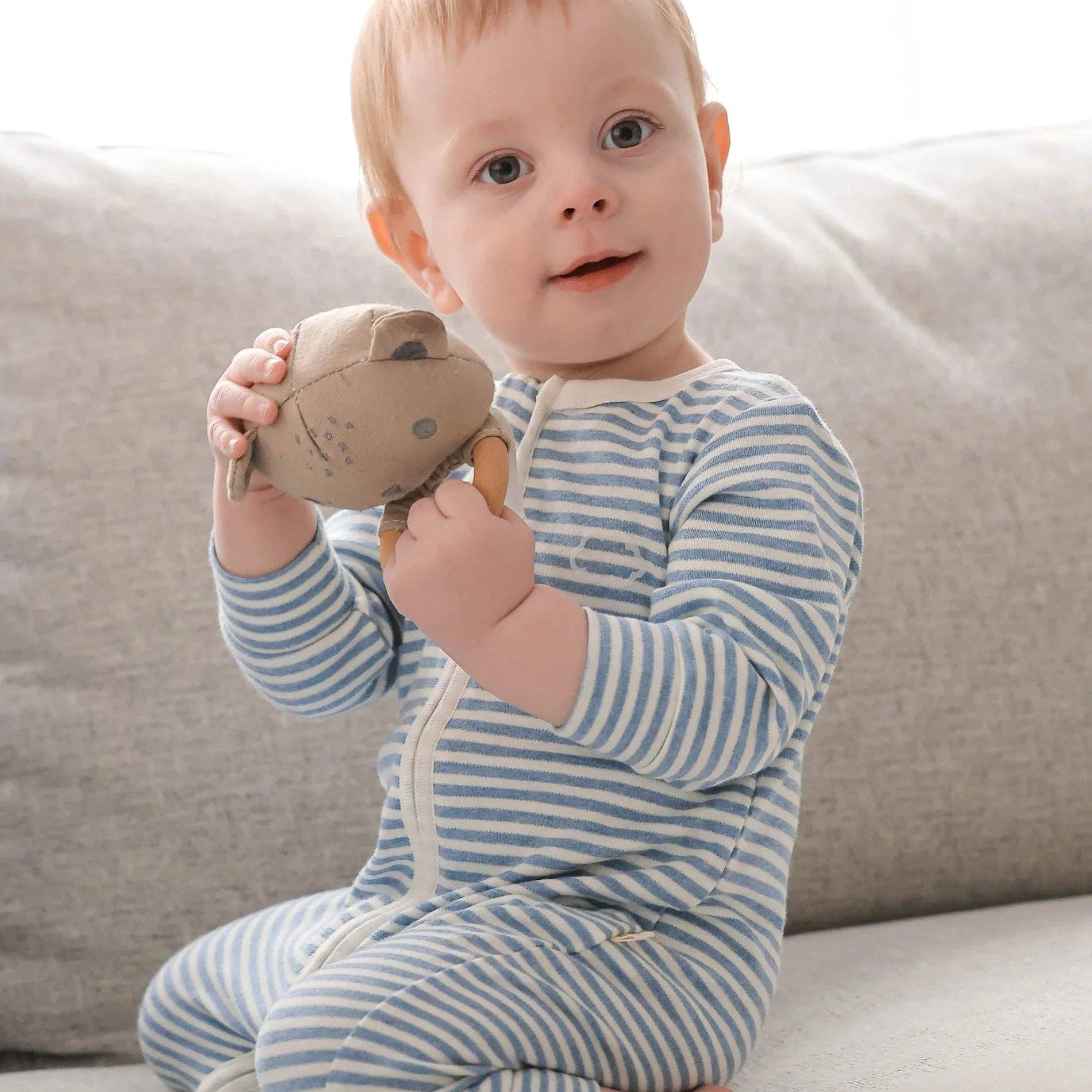 Baby in a striped outfit holding a plush toy on a neutral background