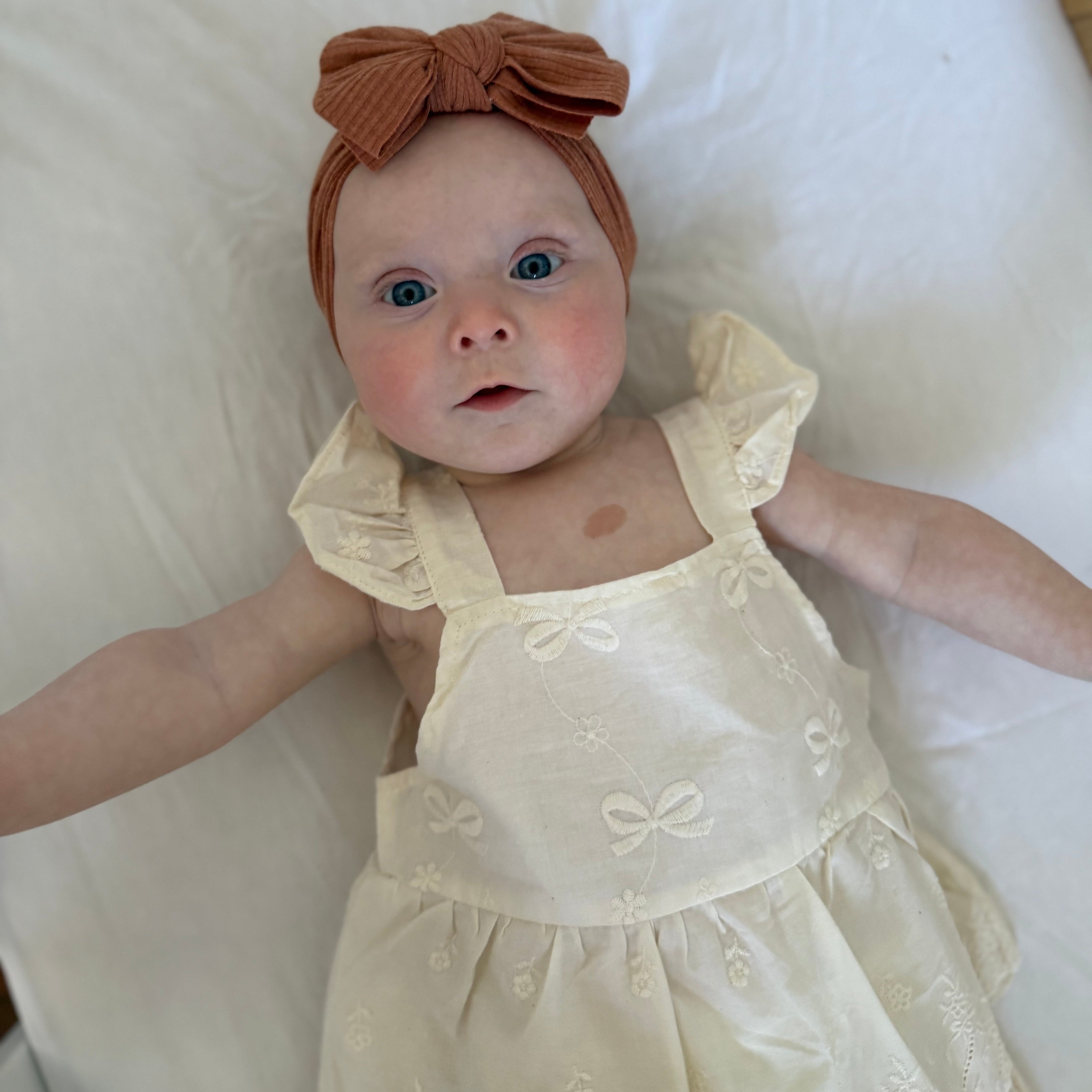 Baby in a yellow dress with a brown bow headband on a white background