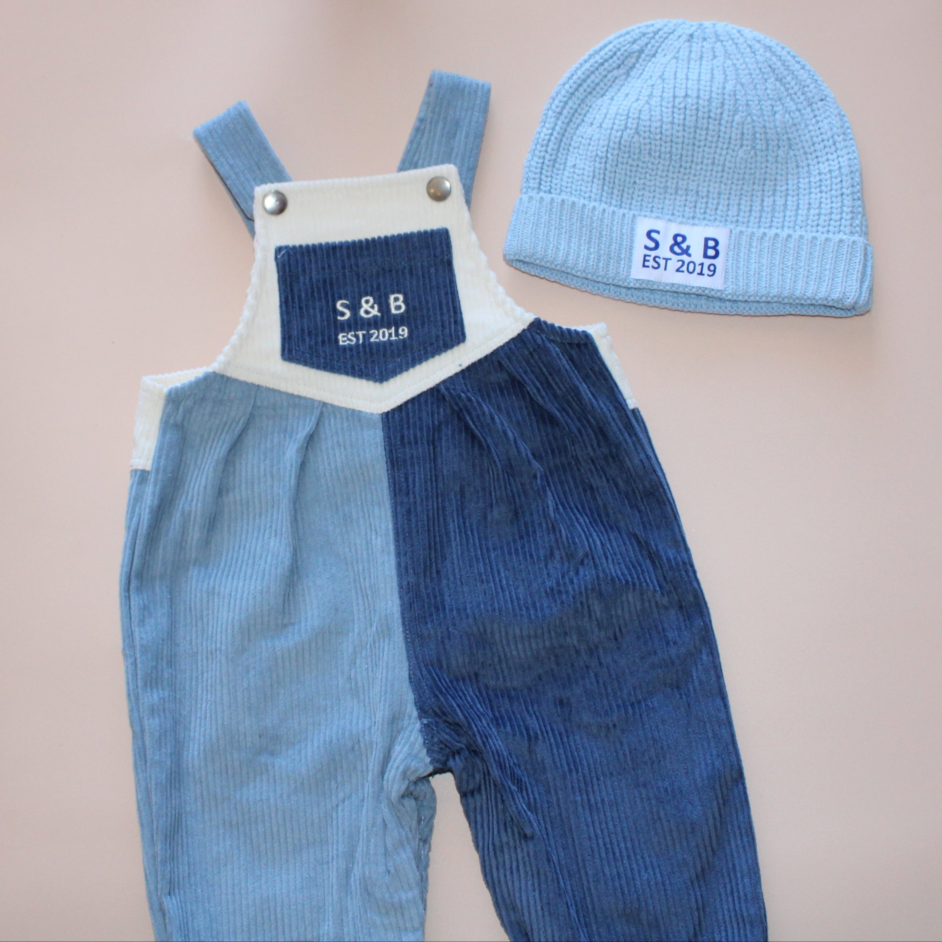 Blue overalls and matching hat on a pink surface with a gray background