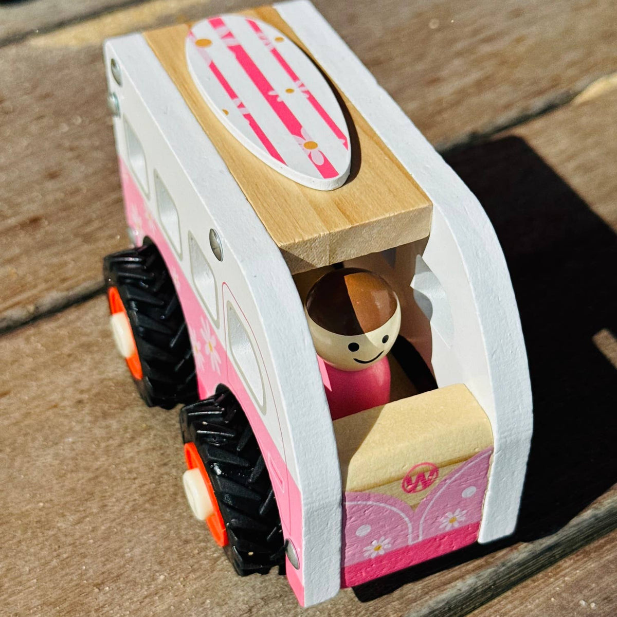 Wooden toy camper with a doll inside on a wooden surface