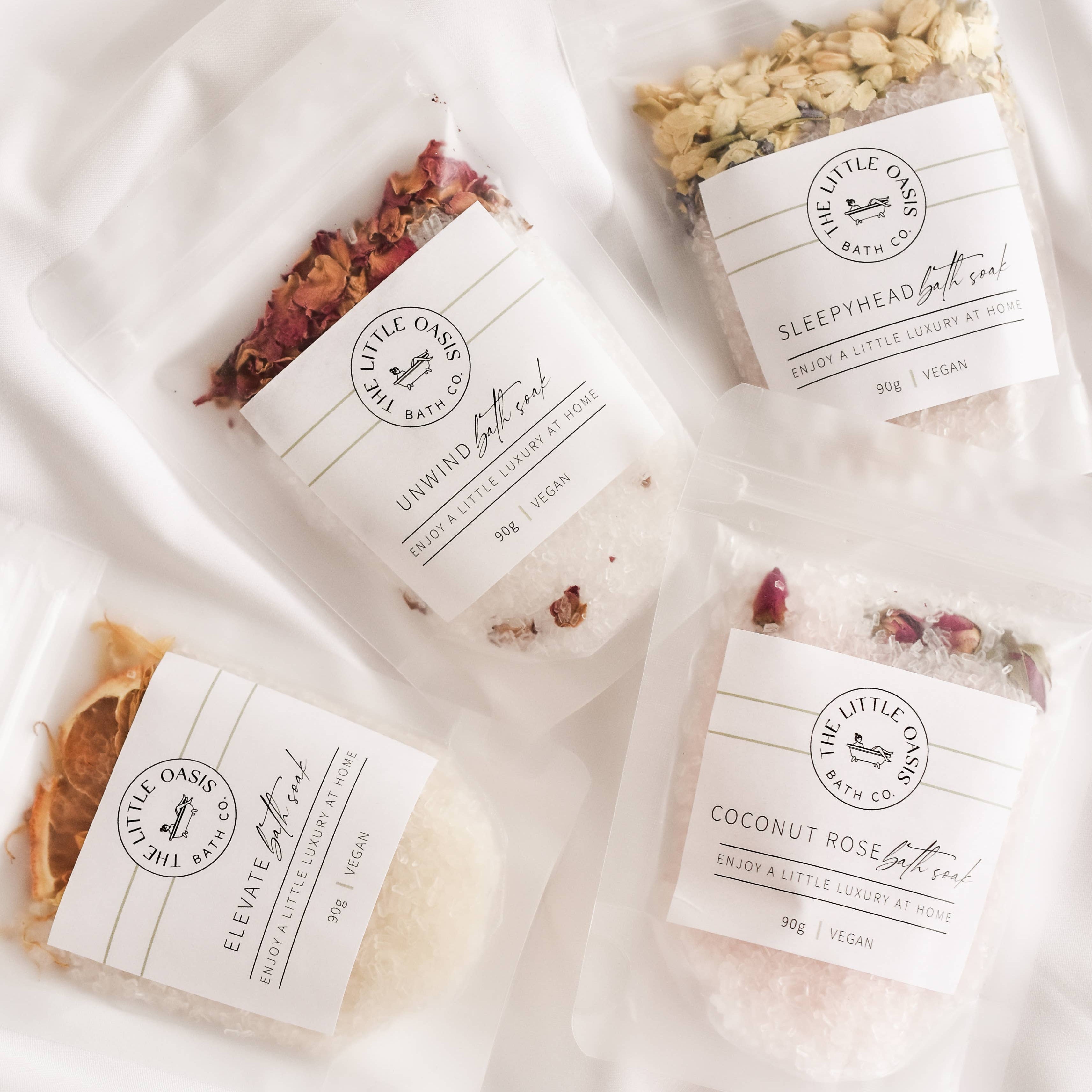 Four packages of bath salts with visible branding on a white fabric background