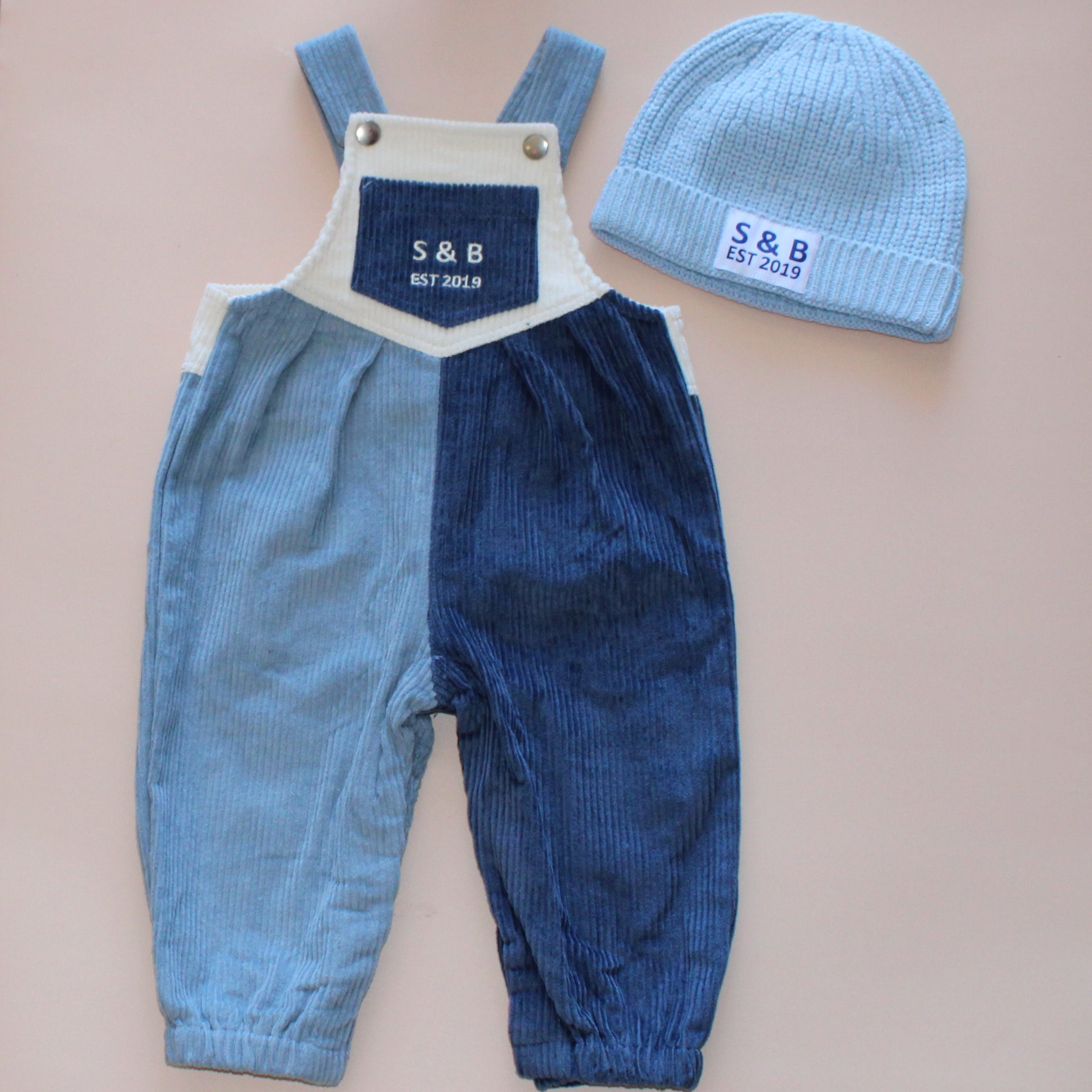 Blue baby overalls and hat on a pink surface with a concrete floor background