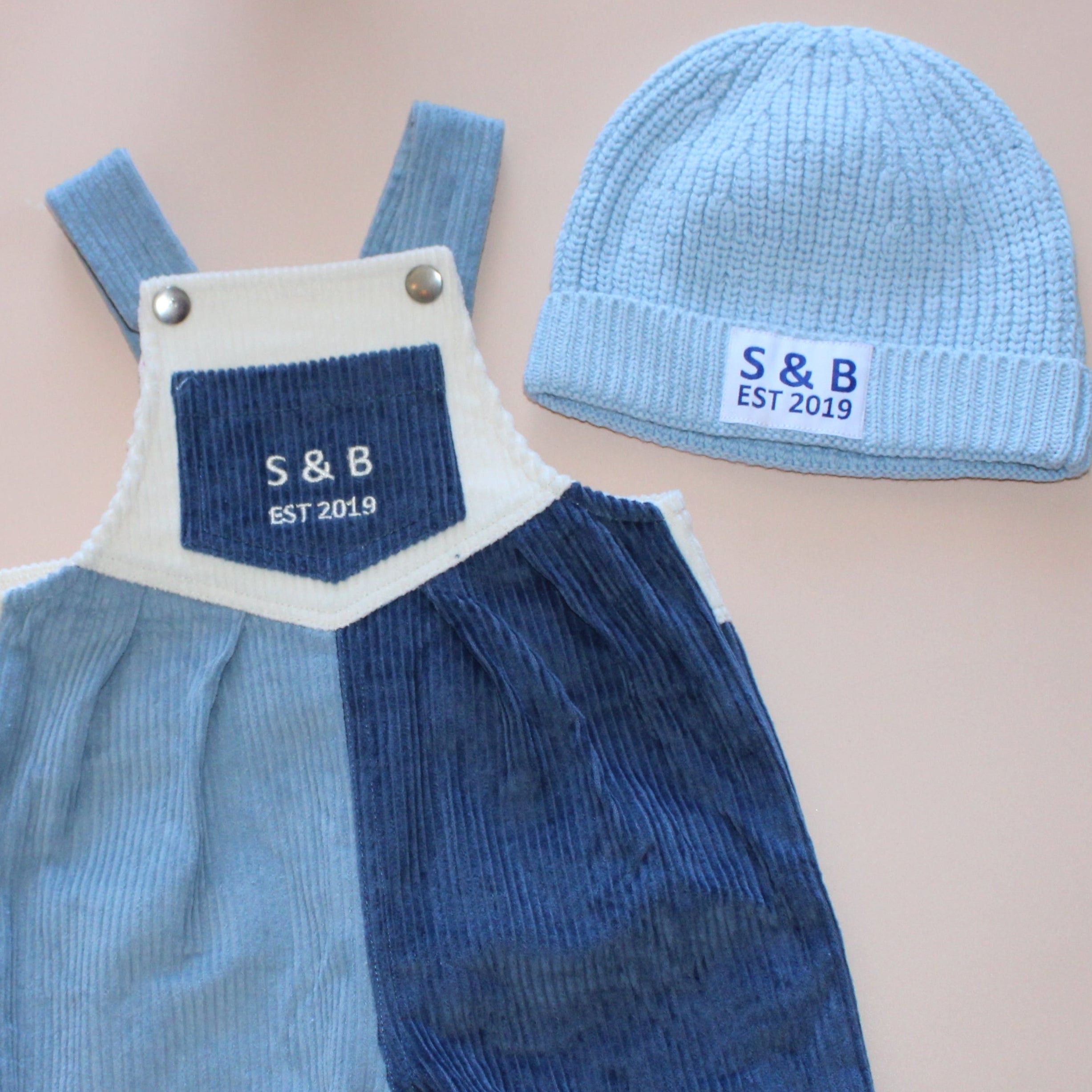 Blue overalls and matching hat on a pink surface with a gray background